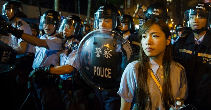 Yau Wai-ching (right) stands in front of riot police outside the Liaison Office after the Chinese legislature effectively barred her from taking her Legco seat. Photo: AFP Yau Wai-ching (right) stands in front of riot police outside the Liaison Office after the Chinese legislature effectively barred her from taking her Legco seat. Photo: AFP
